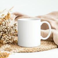 white mug placed on woven mat with dried flowers and soft fabric, creating serene and cozy atmosphere. Perfect for showcasing designs or branding photo