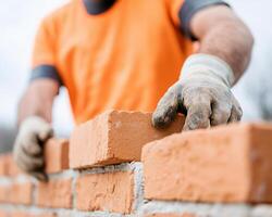 Building brick wall with skilled craftsmanship, worker in orange shirt carefully places bricks, showcasing dedication and precision in construction photo