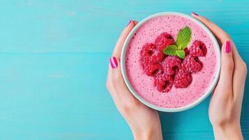 close up of hands holding smoothie bowl filled with vibrant pink raspberry smoothie and fresh raspberries, garnished with mint leaf, evokes refreshing and healthy vibe photo