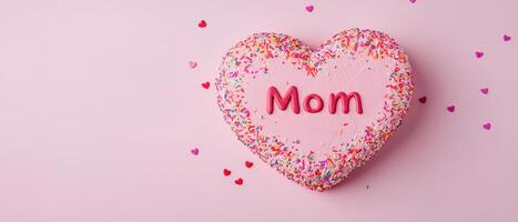 heart shaped cake decorated with pink frosting and colorful sprinkles celebrates Mother Day with word Mom prominently displayed photo