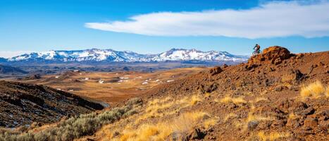 mountain biker rides on rocky terrain with snow capped mountains in background, showcasing stunning landscape photo