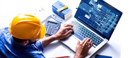 construction worker using laptop to manage project plans and data photo