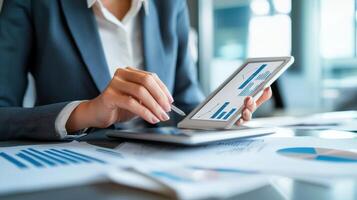Focused businesswoman analyzing graphs on digital tablet, surrounded by reports and charts, showcasing her analytical skills photo