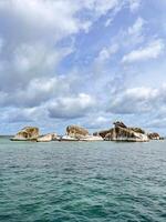 A group of rocks in the ocean with a cloudy sky photo