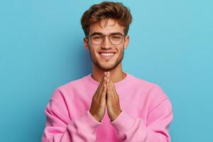 Young man smiling with hands together against blue background in casual attire photo