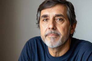 Middle-aged man with gray hair and beard showing calm expression in neutral background indoors photo