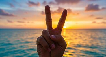 A hand displaying the peace sign against a sunset sky photo