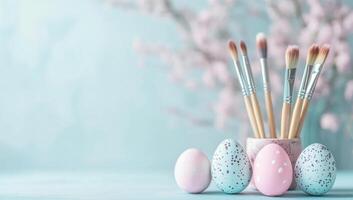 Pastel-colored easter eggs with delicate dotting, paintbrushes, and flowering branch resting against soft blue surface photo