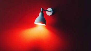 White wall lamp is casting a warm glow on a textured, red wall, adding a touch of brightness to the room photo
