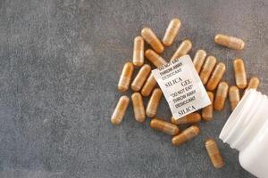 Gel capsules and silica gel packets scattered on a gray surface photo