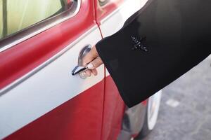Hand reaching for car door on a vintage red vehicle at midday photo