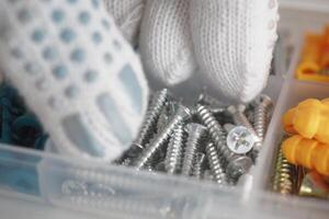 Screws and fasteners sorted in a storage container with gloved hands photo