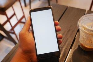 Hand holding a smartphone on a table in a cafe setting photo
