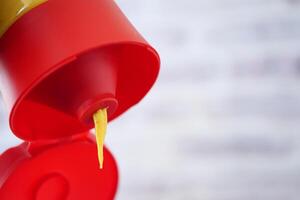 Squeezing mustard from a bottle with a red cap and yellow condiment photo