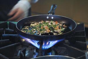 Cooking vegetables in a frying pan over a gas flame photo
