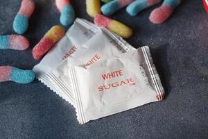 Sugar packets and colorful gummy candies on a dark surface photo