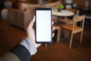 Empty smartphone held in hand inside a cozy cafe setting photo