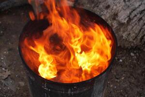 Fire blazing in a metal container outdoors during daylight hours photo