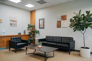 A waiting room with a couch, a table, and a plant photo