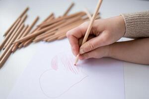 Female hand drawing heart with colored pencils on white paper photo
