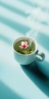 Minimalistic flat lay of white ceramic cup with flower and tea on blue background photo