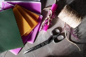 Colorful wax sheets with scissors twine and wrapped candle on a stone surface photo