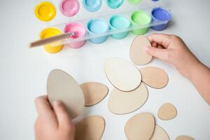 Child painting wooden Easter eggs with colorful paints photo