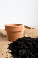 Empty terracotta pot with soil on craft paper against white background photo