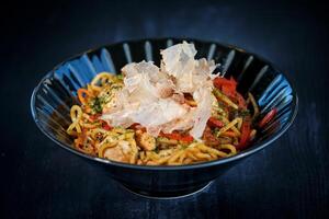Appetizing noodles in bowl with crisps placed on black table photo