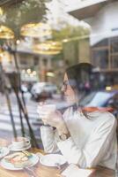 A woman sitting at a table in front of a window while had a sip of coffee photo