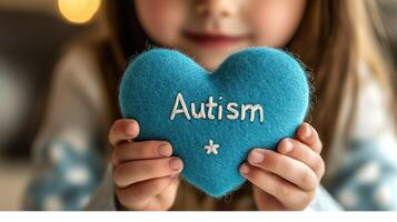 A child holds a blue felt heart with 'Autism' written on it. photo