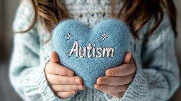 A child holding a soft blue heart with 'Autism' inscribed on it. photo