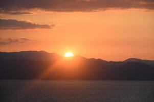 Golden sunset casts a warm glow over tranquil mountains and serene waters in a picturesque landscape photo