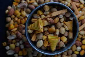 Colorful snack mix in a silver bowl surrounded by a variety of nuts and crunchy bites on a dark wooden surface photo