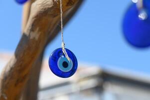 Bright blue glass talisman catches sunlight while hanging from a twisted branch against a clear sky photo