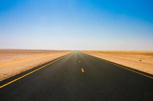 An empty road in the desert with a blue sky photo