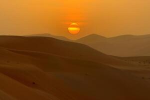 A desert scene with a sun setting over the sand photo