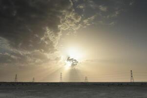 A man standing in the desert with a sun shining through the clouds photo