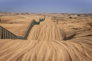 A fence in the desert with sand dunes in the background photo