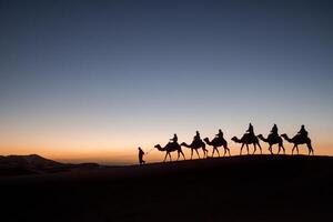 A group of people on camels are walking across the desert photo
