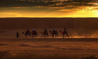 A group of people riding camels in the desert photo