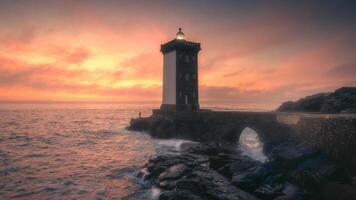 A lighthouse stands on the shore of the ocean at sunset photo
