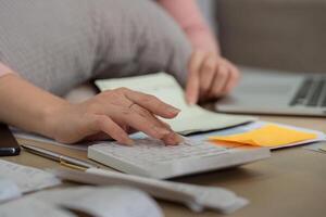 Financial Calculations and Expense Management. Close-up of a woman calculating her expenses with a calculator amidst financial documents and a laptop. photo