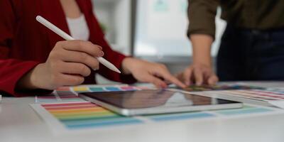 Digital Creation and Design Process. A close-up of a designer's hand using a stylus on a tablet alongside vibrant color charts. photo