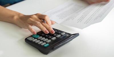 Financial Management and Saving Strategies. A person calculating expenses with a calculator while reviewing financial documents. photo