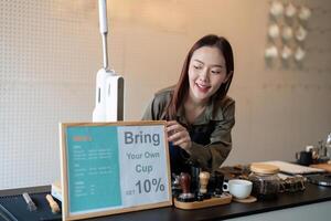 Promoting Eco-Conscious Choices. A barista setting up a sign to encourage customers to bring their own cups for discounts. photo