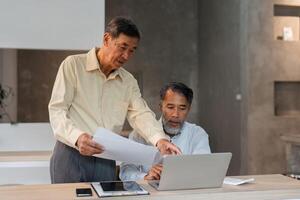 Business Collaboration and Insightful Guidance. Two senior men analyze a laptop screen and documents in a modern workspace. photo