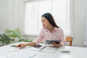Remote Work and Document Review. A woman strategizes her tasks while reviewing papers and utilizing tech tools in her home office. photo