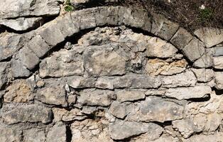 An ancient stone wall with archway provides a textured and historical architectural background. photo