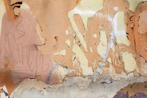 A heavily weathered wall features peeling paint layers, creating a textured, abstract surface. photo